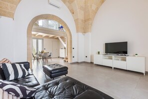 Ein modernes Wohnzimmer mit einer Ledersofa, einem Flachbildfernseher auf einem weißen Schrank und einem Essbereich im Hintergrund.
