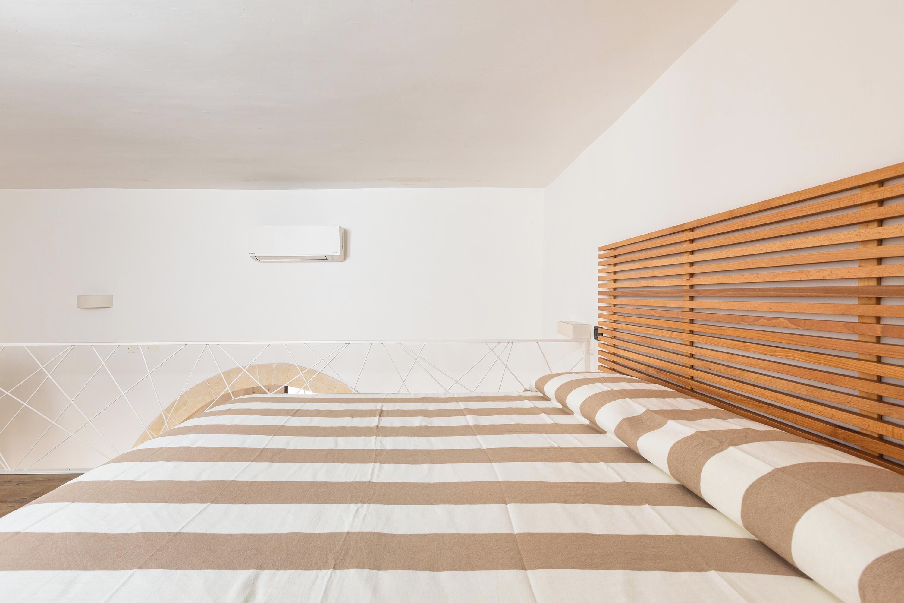 Ein Schlafzimmer mit einem Bett, einem Holzlatten-Kopfstück und einem geometrischen Wanddesign.