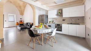 Une cuisine moderne avec des meubles blancs, un coin repas doté d’une table ronde et un salon avec un canapé noir.