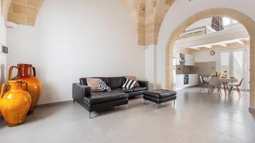 Un salon moderne avec un canapé en cuir noir, une table basse et un grand vase. Un arc donne accès à la cuisine et à la salle à manger.