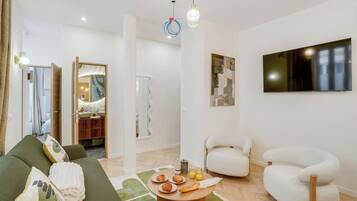 A modern living room with a sofa, chairs, a coffee table with pastries, and a TV on the wall.