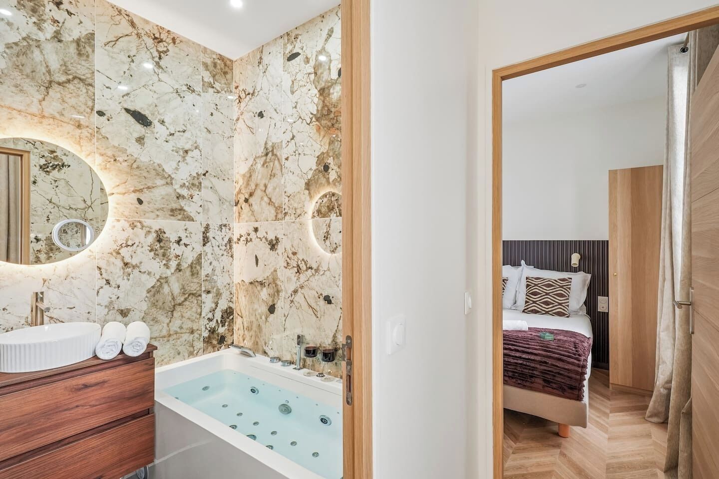 A modern bathroom with a marble wall, a bathtub, and a vanity with a mirror.