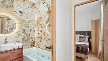 A modern bathroom with a marble wall, a bathtub, and a vanity with a mirror.