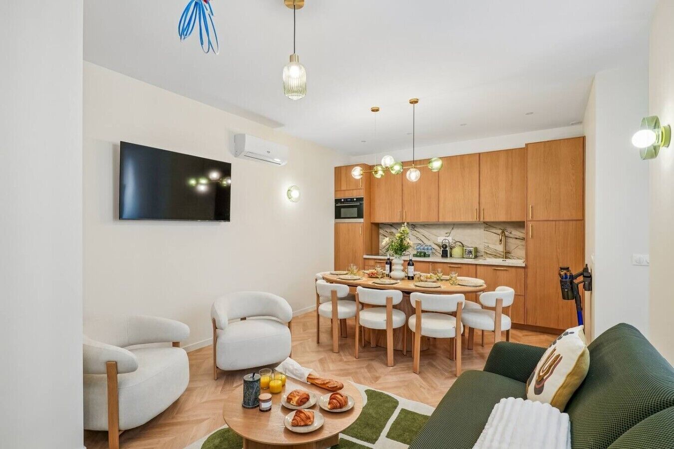 Ein modernes Wohnzimmer mit Essbereich, einem an der Wand befestigten Flachbildfernseher und einer Küche mit Holzschränken und einer Marmor-Spritzwand.