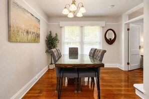 A dining room with a glass-top table, upholstered chairs, a potted plant, and a painting on the wall. - 3BR Home | Prime Lake Hollingsworth | Dog Friendly (Lakeland)