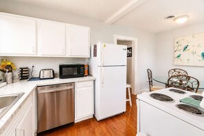 A compact kitchen with white cabinets, a stainless steel dishwasher, a white refrigerator, a microwave, and a stove with four burners. - 3BR Home | Prime Lake Hollingsworth | Dog Friendly (Lakeland)