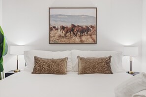 Ett hotellrum med en säng, två lampor och en inramad tavla med hästar på väggen.
