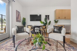 Ein modernes Wohnzimmer mit Essbereich, einem an der Wand befestigten Flachbildfernseher und einer Küche mit Holzschränken.