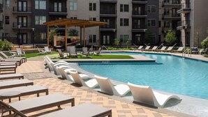 A swimming pool with lounge chairs and a covered seating area, surrounded by apartment buildings. - Comfortable 1BR Retreat at The Nelson TNS 5205 (Austin)