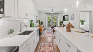 A modern kitchen with white cabinetry, a central island, and a dining area with a view to the outdoors. - Comfortable 1BR Retreat at The Nelson TNS 5205 (Austin)