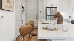 A modern kitchen with white cabinetry, a stainless steel refrigerator, a dining area with a large island, and a horse sculpture centerpiece. - Comfortable 1BR Retreat at The Nelson TNS 5205 (Austin)
