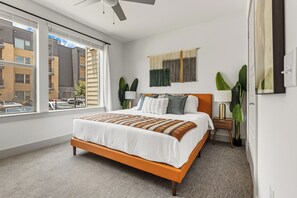 A modern bedroom with a large bed, a view of the city, and a ceiling fan. - Modern 2BR Haven with Balcony & Open Living (Austin)
