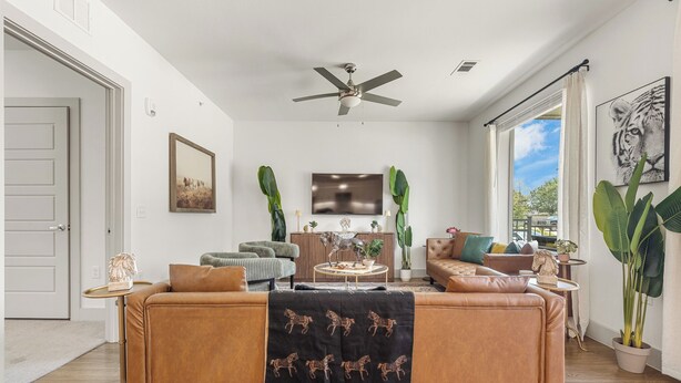Ein Wohnzimmer mit einem großen Sofa, einem Deckenventilator, einem Flachbildfernseher und Blick ins Freie.