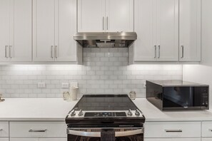 A kitchen with white cabinets, a stainless steel range hood, a black induction cooktop, and a black microwave. - Modern 2BR Haven with Balcony & Open Living (Austin)