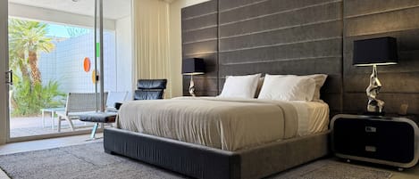 A modern bedroom with a large bed, a ceiling fan, a nightstand, and a view of the outdoors.