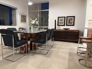 Uma área de refeições moderna com uma mesa de vidro, cadeiras com padrão preto e branco, um armário de madeira e obras de arte emolduradas na parede.