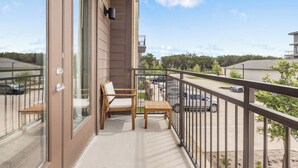 A balcony with a wooden chair and table, a glass door, and a view of a parking area and buildings. - Relaxed 1BR Apartment Stay at The Nelson TNS 4204 (Austin)