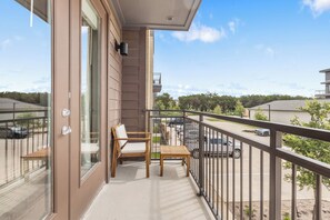 A balcony with a wooden chair and table, a glass door, and a view of a parking area and buildings. - Relaxed 1BR Apartment Stay at The Nelson TNS 4204 (Austin)