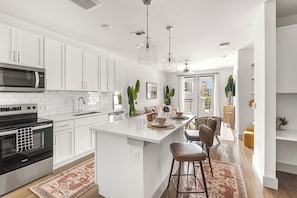 A modern kitchen with white cabinetry, a central island with bar stools, a built-in oven, and a microwave. - Relaxed 1BR Apartment Stay at The Nelson TNS 4204 (Austin)