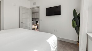 A bedroom with a bed, a television on the wall, a door leading to a bathroom, and a potted plant. - Relaxed 1BR Apartment Stay at The Nelson TNS 4204 (Austin)