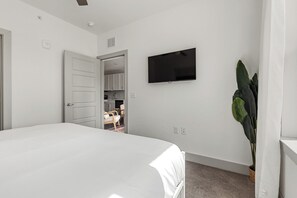 A bedroom with a bed, a television on the wall, a door leading to a bathroom, and a potted plant. - Relaxed 1BR Apartment Stay at The Nelson TNS 4204 (Austin)