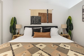 A bedroom with a bed, two nightstands, a wall tapestry, and two potted plants. - Studio-Style 1BR Retreat at The Nelson (Austin)