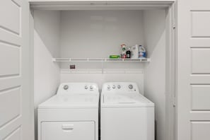 Een wasserette met twee wasmachine-droger combinaties en een plank daarboven met schoonmaakmiddelen.