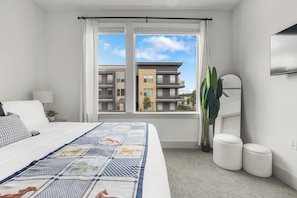A bedroom with a large bed, a window with curtains, a flat-screen TV, and a potted plant. - Stylish 2BR Apartment for Work & Relaxing TNS 4202 (Austin)