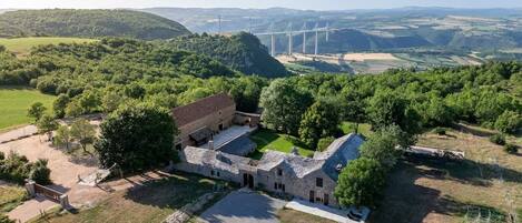 Une vue aérienne d’un bâtiment historique en pierre, doté d’une cour intérieure, entouré d’une végétation luxuriante et avec un pont en arrière-plan.