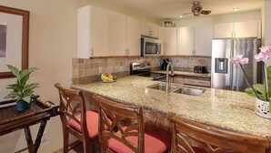 A modern kitchen with granite countertops, stainless steel appliances, and a central island with bar stools. - Ocean View 4BR, 2 Condos for 12 in Kihei! (Kihei)