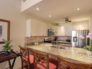 A modern kitchen with granite countertops, stainless steel appliances, and a central island with bar stools. - Ocean View 4BR, 2 Condos for 12 in Kihei! (Kihei)
