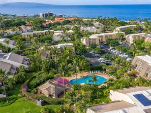 A resort with a swimming pool surrounded by lush greenery and palm trees, with a view of the ocean. - Kihei, Maui Kamaole, Spacious 4 BR, Ocean View, Sleeps 12 (Kihei)