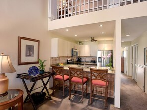 A modern kitchen with a central island, overhead lighting, and a view to a balcony. - Kihei, Maui Kamaole, Spacious 4 BR, Ocean View, Sleeps 12 (Kihei)