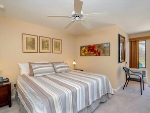 A bedroom with a bed, a desk, a chair, a ceiling fan, and artwork on the walls. - Ocean View 4BR, 2 Condos for 12 in Kihei! (Kihei)