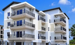 A multi-story residential building with balconies, air conditioning units, and a clear sky.