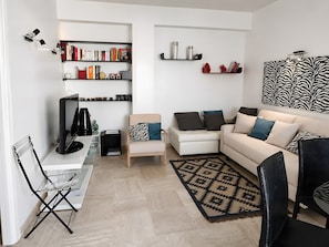 Ein modernes Wohnzimmer mit einem weißen Sofa, einem schwarzen Sessel, einem Bücherregal und Wandkunst mit Zebra-Muster.