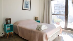 Una camera da letto con un letto, un comodino, un quadro appeso al muro e una finestra con tende.