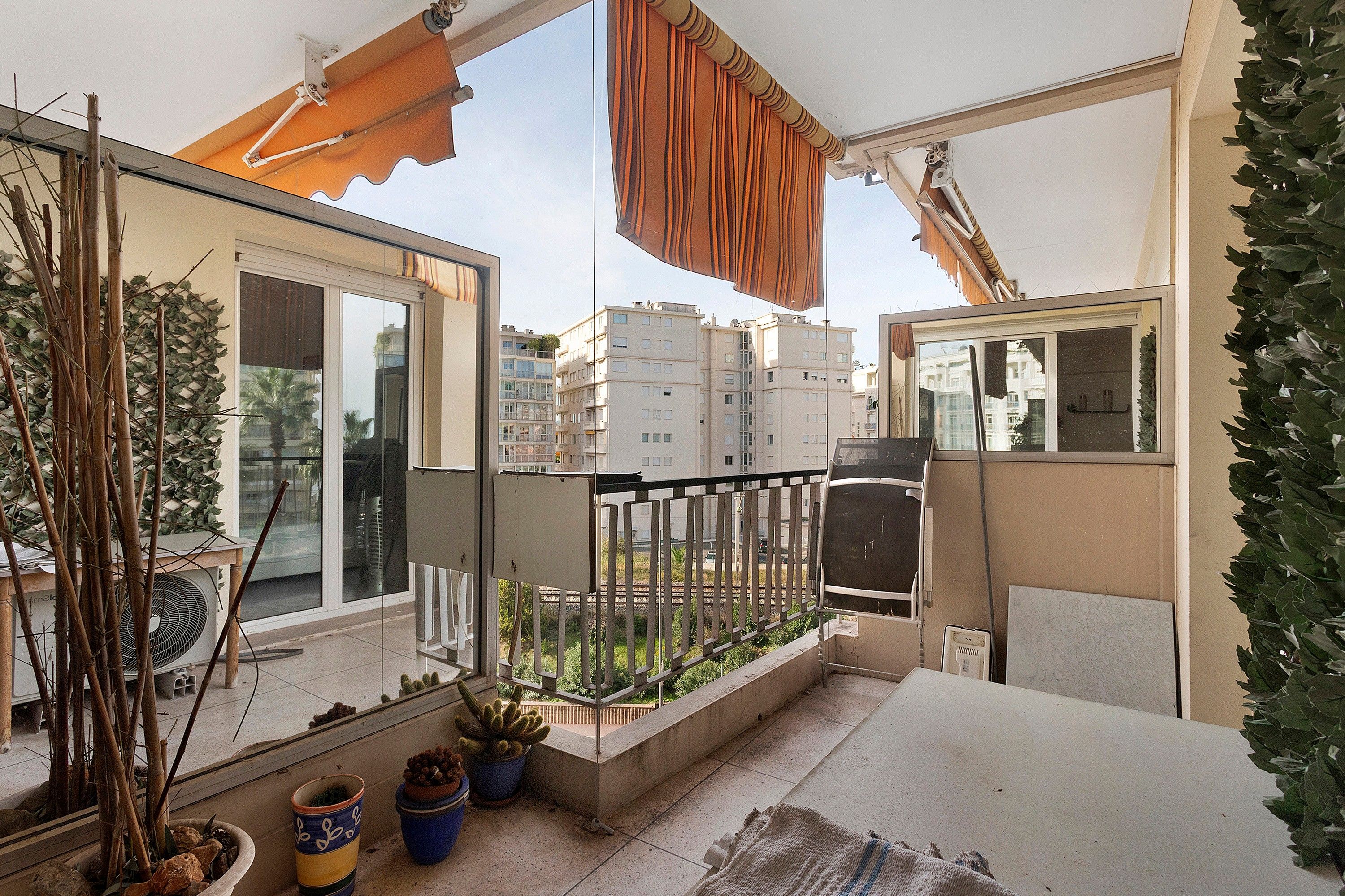 A balcony with potted plants, a window, and a view of surrounding buildings.