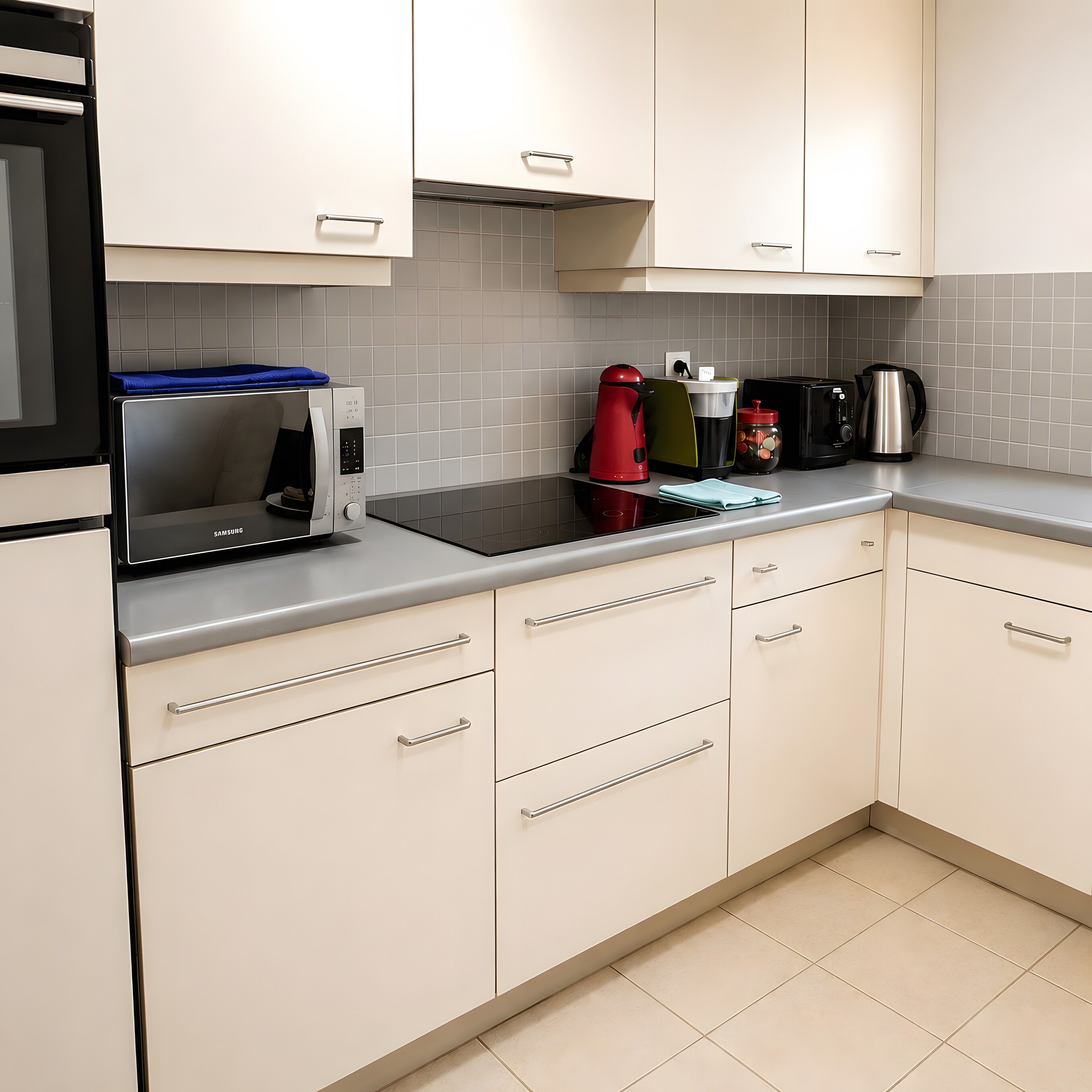A kitchen with white cabinets, a black microwave, a red kettle, and a coffee maker on the counter.