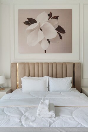 A neatly made bed with white linens and pillows, a beige upholstered headboard, and a large floral artwork above it. - Beautiful Dubai Marina View 1BR - Walk to Beach & Metro (Dubai)