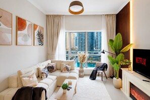 A modern living room with a sofa, coffee table, TV, and a view of a cityscape. - Beautiful Dubai Marina View 1BR - Walk to Beach & Metro (Dubai)