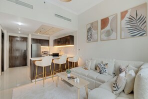 A modern living room with a sofa, a coffee table, and a kitchen area with a dining table and chairs. - Beautiful Dubai Marina View 1BR - Walk to Beach & Metro (Dubai)