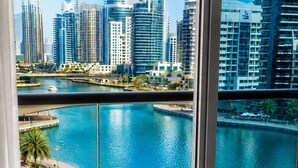A modern hotel room with a balcony overlooking a marina and city skyline. - Beautiful Dubai Marina View 1BR - Walk to Beach & Metro (Dubai)
