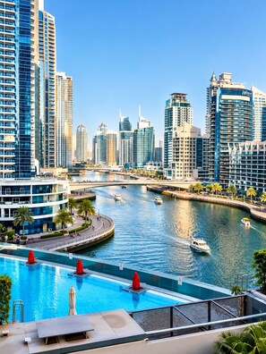 A modern hotel with a pool, overlooking a marina with boats and a city skyline. - Beautiful Dubai Marina View 1BR - Walk to Beach & Metro (Dubai)