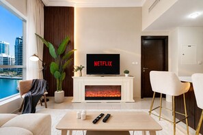 A modern living room with a fireplace, a television displaying 'NETFLIX,' and a view of a body of water. - Beautiful Dubai Marina View 1BR - Walk to Beach & Metro (Dubai)