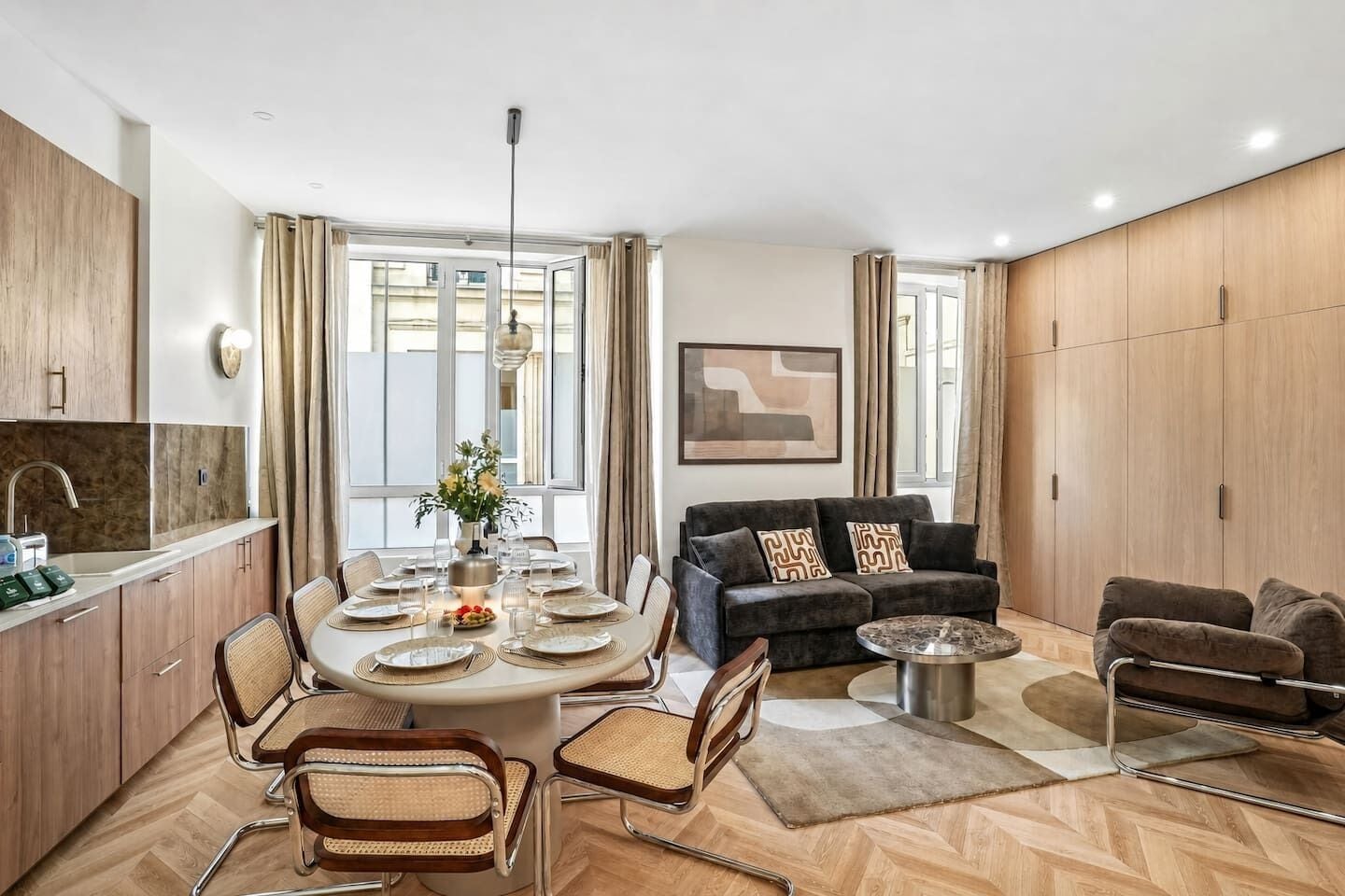 A modern living room with a dining area, wooden cabinets, and a large window.