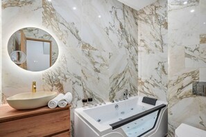 Ein Badezimmer mit Marmorwand, einem runden Spiegel, einem Waschbecken, einer Badewanne und einer Toilette.
