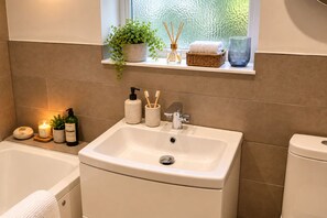 A bathroom with a white sink, a bathtub, and a toilet. There is a shelf above the sink with a plant, a candle, and a glass. - A stylish apartment providing a peaceful base for exploring Hebden Bridge. (Hebden Bridge)