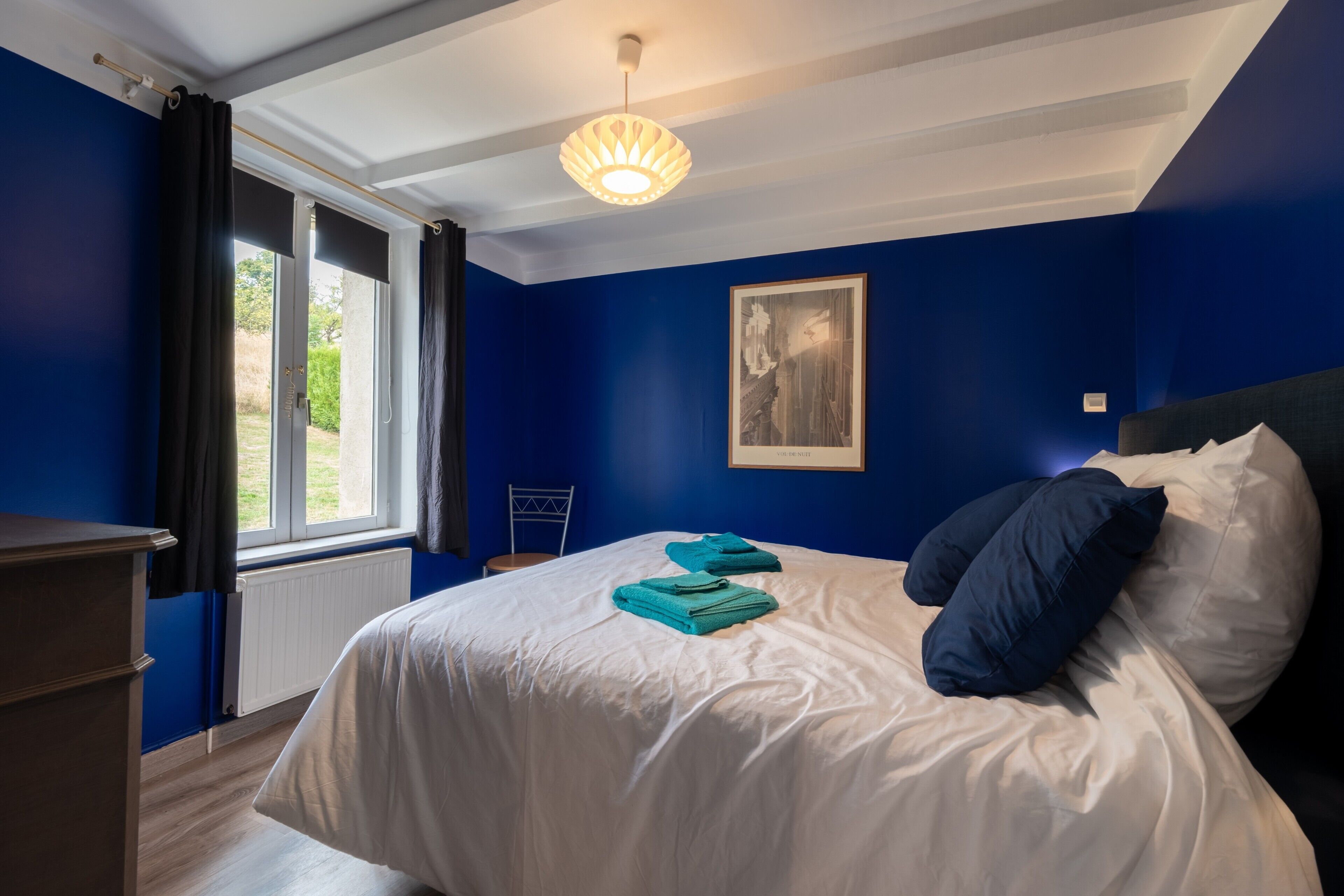 Une chambre à coucher avec un lit, une fenêtre, un tableau et un radiateur.
