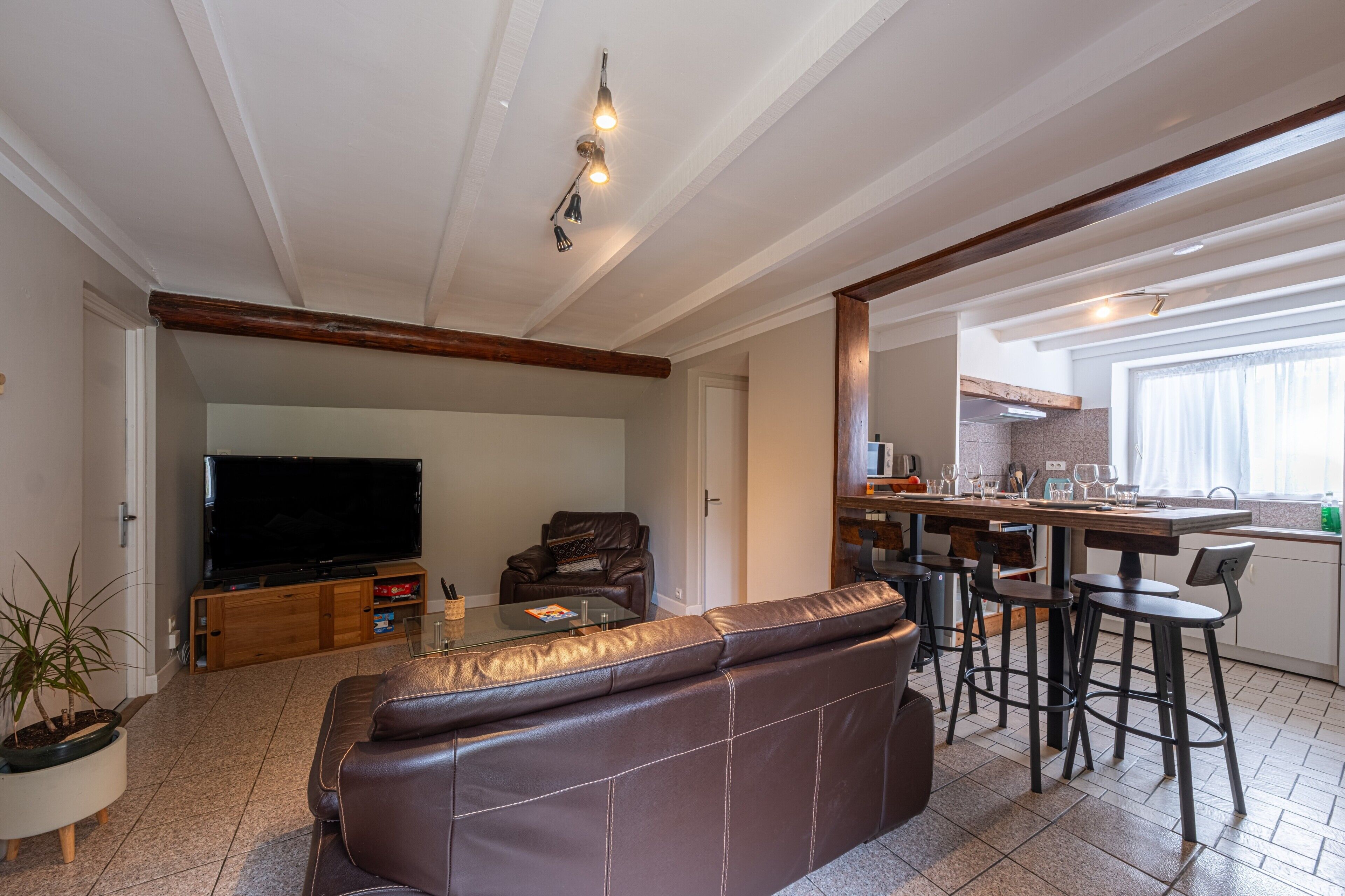 Un salon moderne avec un canapé en cuir, un téléviseur à écran plat et un coin repas équipé de tabourets de bar.